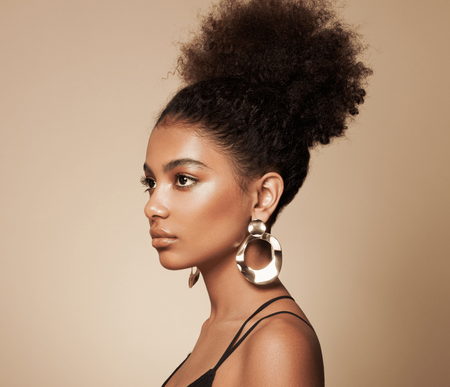 Prepare to be captivated by the allure of a young black woman flaunting a gorgeous afro hairstyle, accentuated by dazzling gold earrings and a flawless natural makeup.